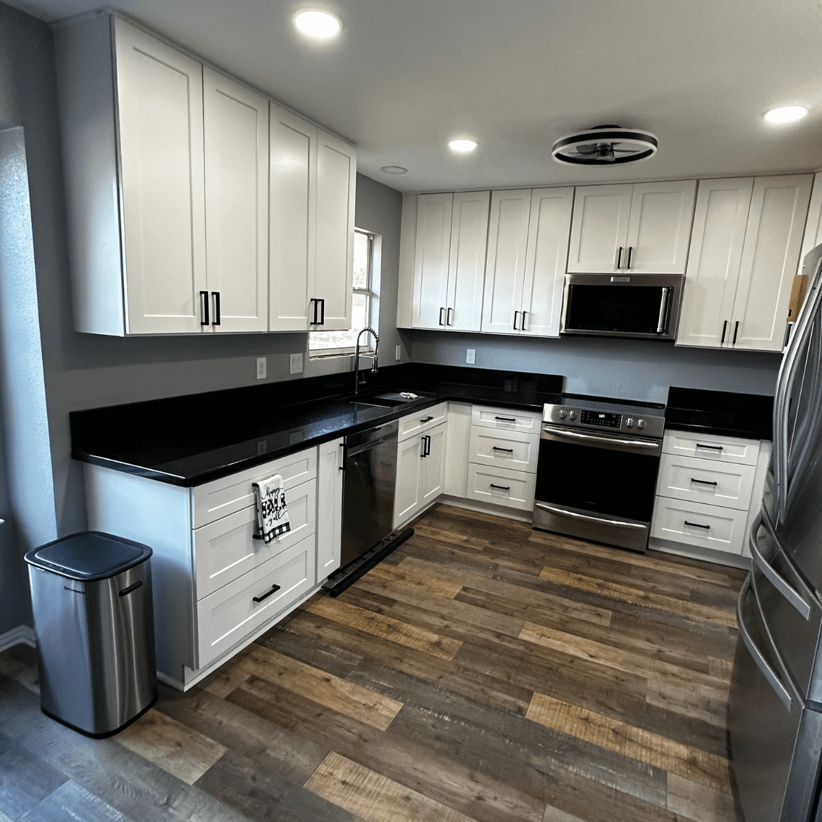 Modern kitchen with white cabinets, black countertops, stainless steel appliances, and wood flooring, exemplifying a recent kitchen remodeling project by a DFW contractor.| Korrect General Contracting Fort Worth TX