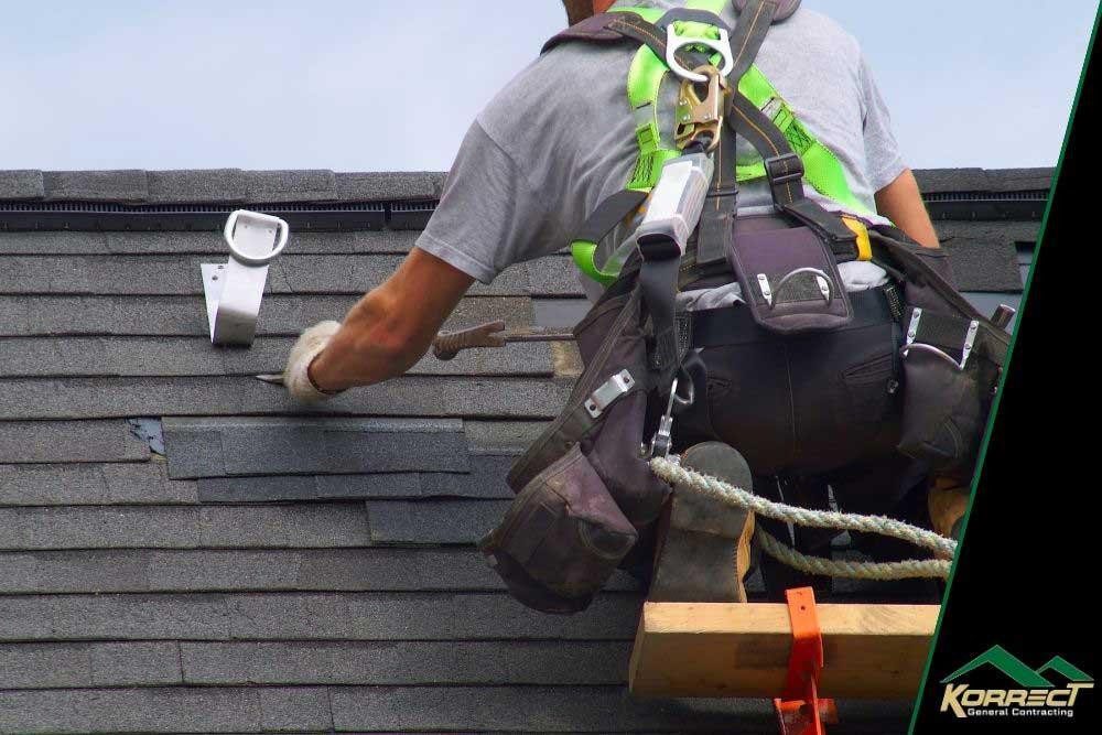Close-up of a roof repair in progress, showing a worker with safety gear fixing asphalt shingles, with the Korrect General Contracting