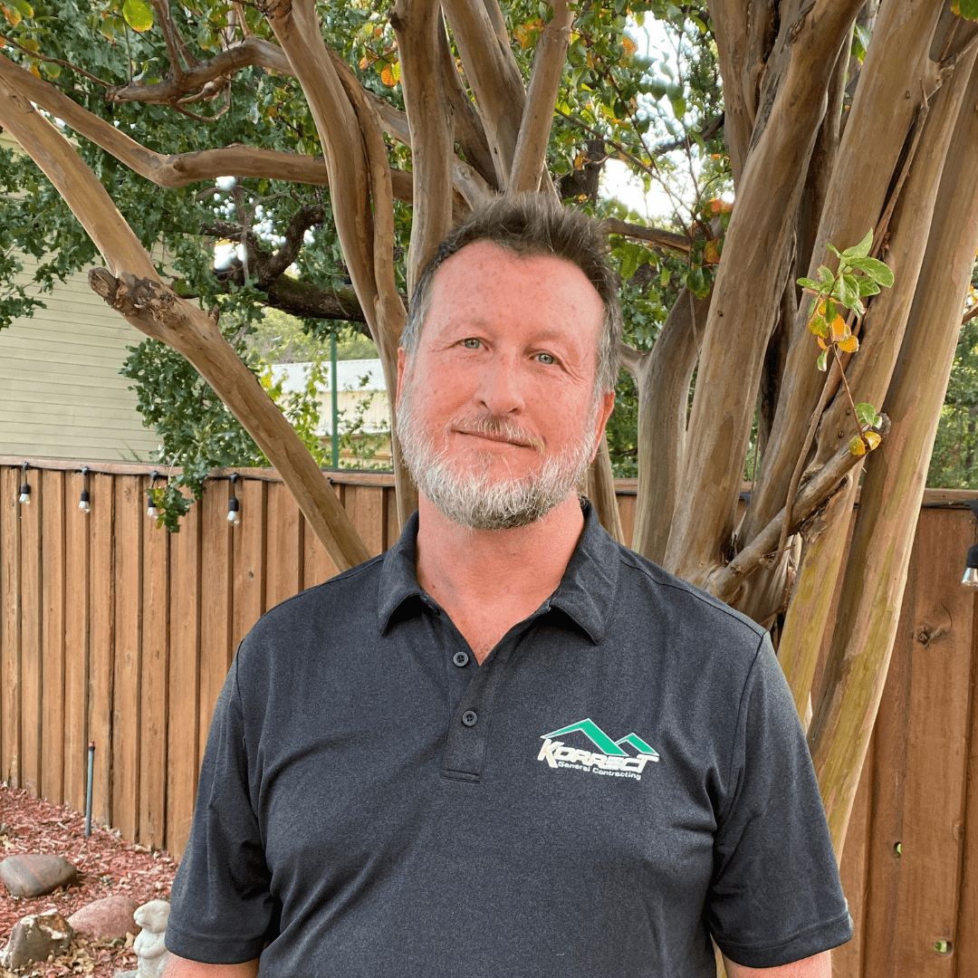 A man in a Korrect General Contracting shirt stands in front of a tree and wooden fence, representing Fort Worth roofing services.| Korrect General Contracting Fort Worth TX